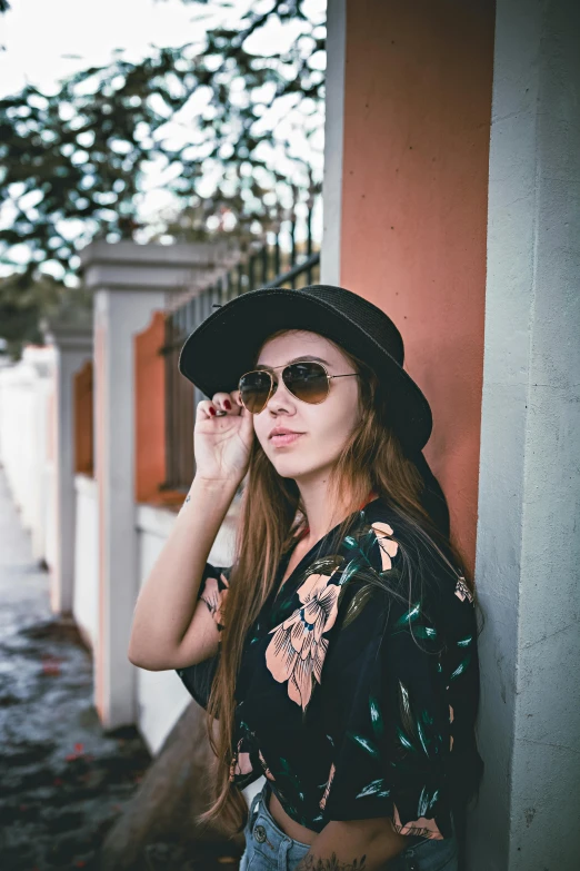 a woman leaning against a wall wearing a hat and sunglasses, shot with premium dslr camera, floral clothes, instagram picture, shot on sony a 7
