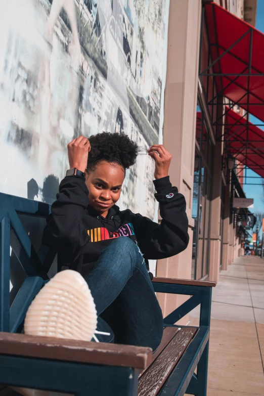 a woman sitting on a bench in front of a wall, by Washington Allston, trending on unsplash, black arts movement, dressed black hoodie, sitting on a store shelf, natural hair, instagram picture