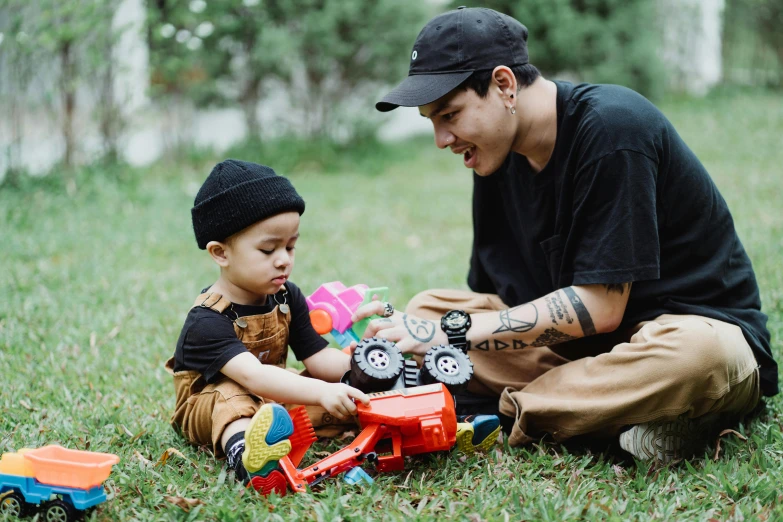 a man playing with a child in the grass, pexels contest winner, realism, kenny wong x pop mart, tattooed, trucks, avatar image