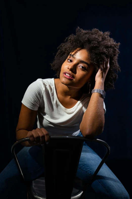 a woman sitting on top of a metal chair, a portrait, by Leo Michelson, pexels contest winner, black young woman, acting headshot, light behind, with textured hair and skin