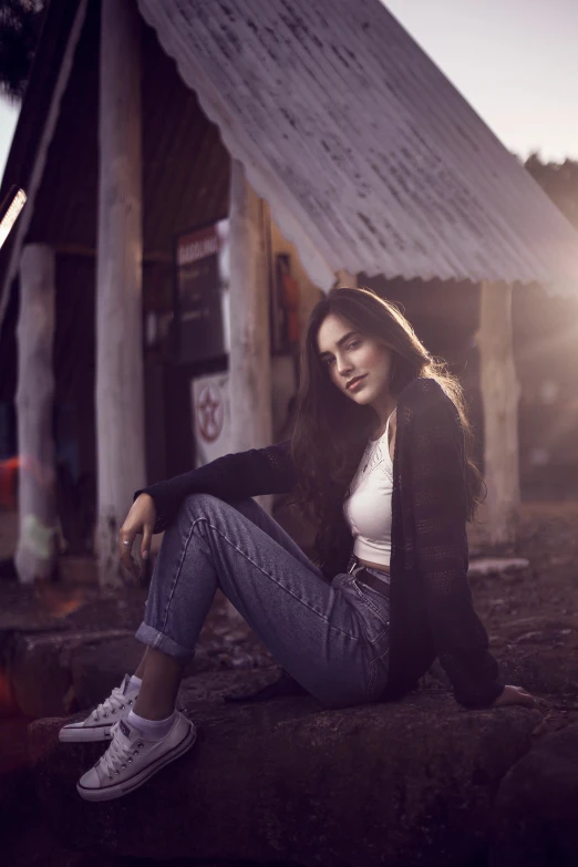 a woman sitting on the ground in front of a building, inspired by Rudy Siswanto, pexels contest winner, sumatraism, handsome girl, cold lighting, stood outside a wooden cabin, young woman with long dark hair