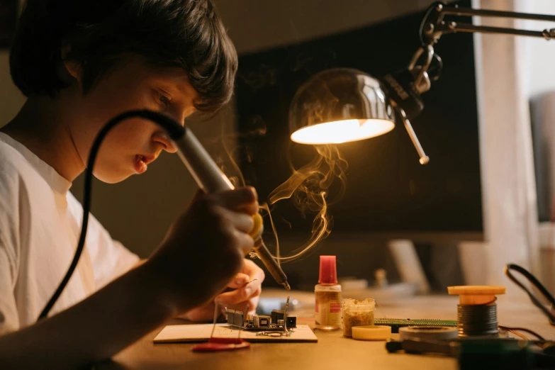 a person sitting at a table working on something, pexels contest winner, process art, smoking soldering iron, light over boy, regular build, experimenting in her science lab