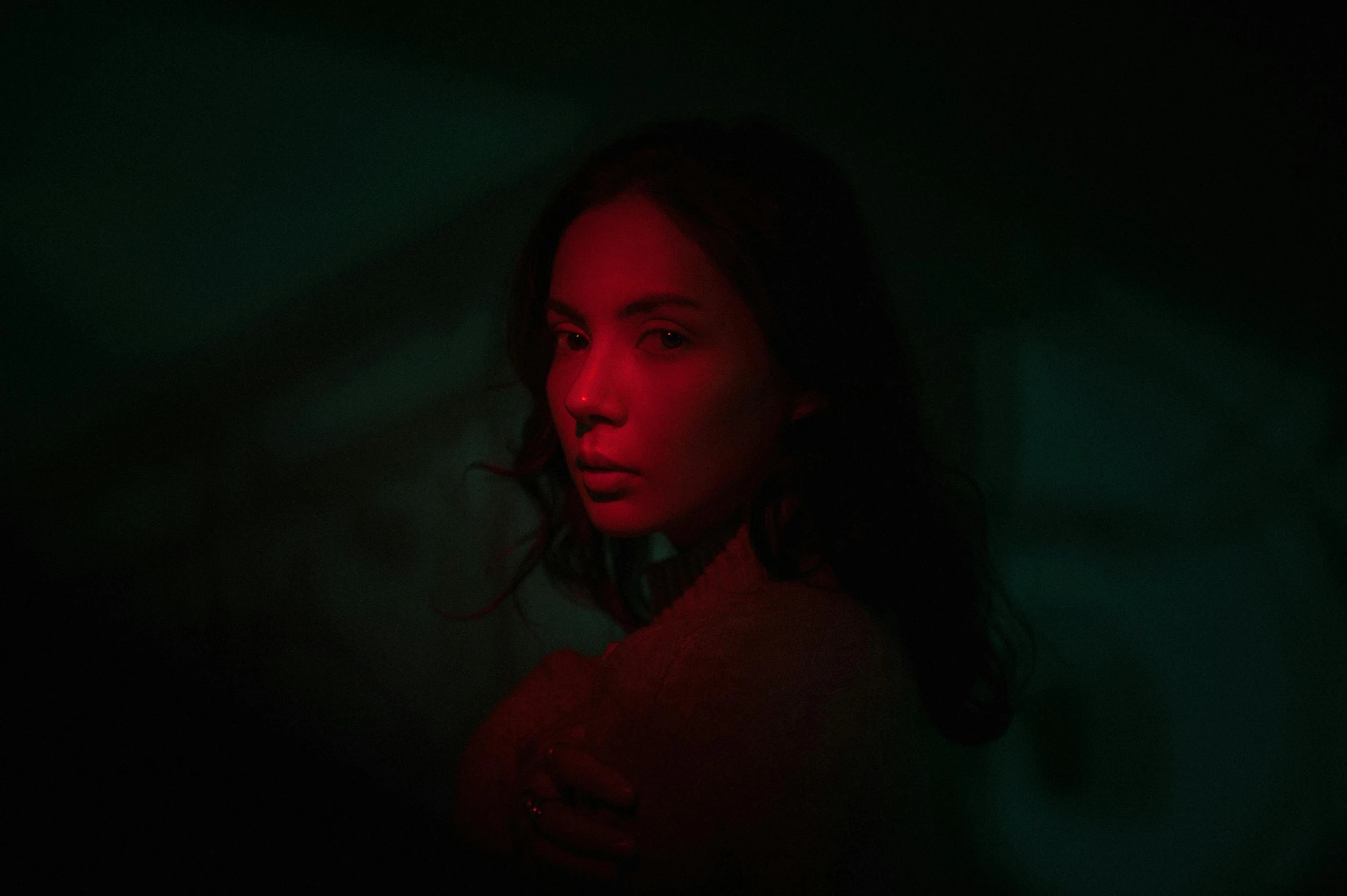 a woman standing in the dark with a red light on her face, an album cover, inspired by Elsa Bleda, pexels contest winner, an asian woman, colored light, light skin, music video