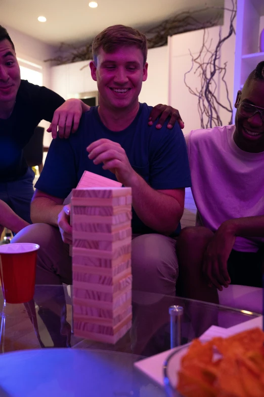 a group of men sitting on top of a couch, jenga tower, bisexual lighting, board games on a table, profile image