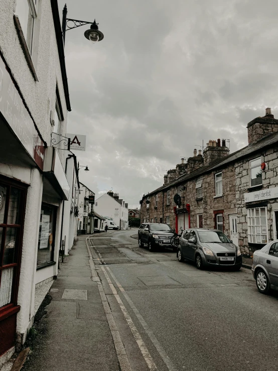 a street with cars parked on the side of it, by Kev Walker, pexels contest winner, pre-raphaelitism, quaint village, trending on vsco, gray skies, 😭 🤮 💕 🎀