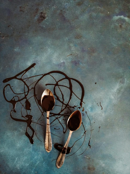 a couple of spoons sitting on top of a table, inspired by Lucio Fontana, trending on unsplash, abstract expressionism, some chocolate sauce, thumbnail, rusting, teal aesthetic