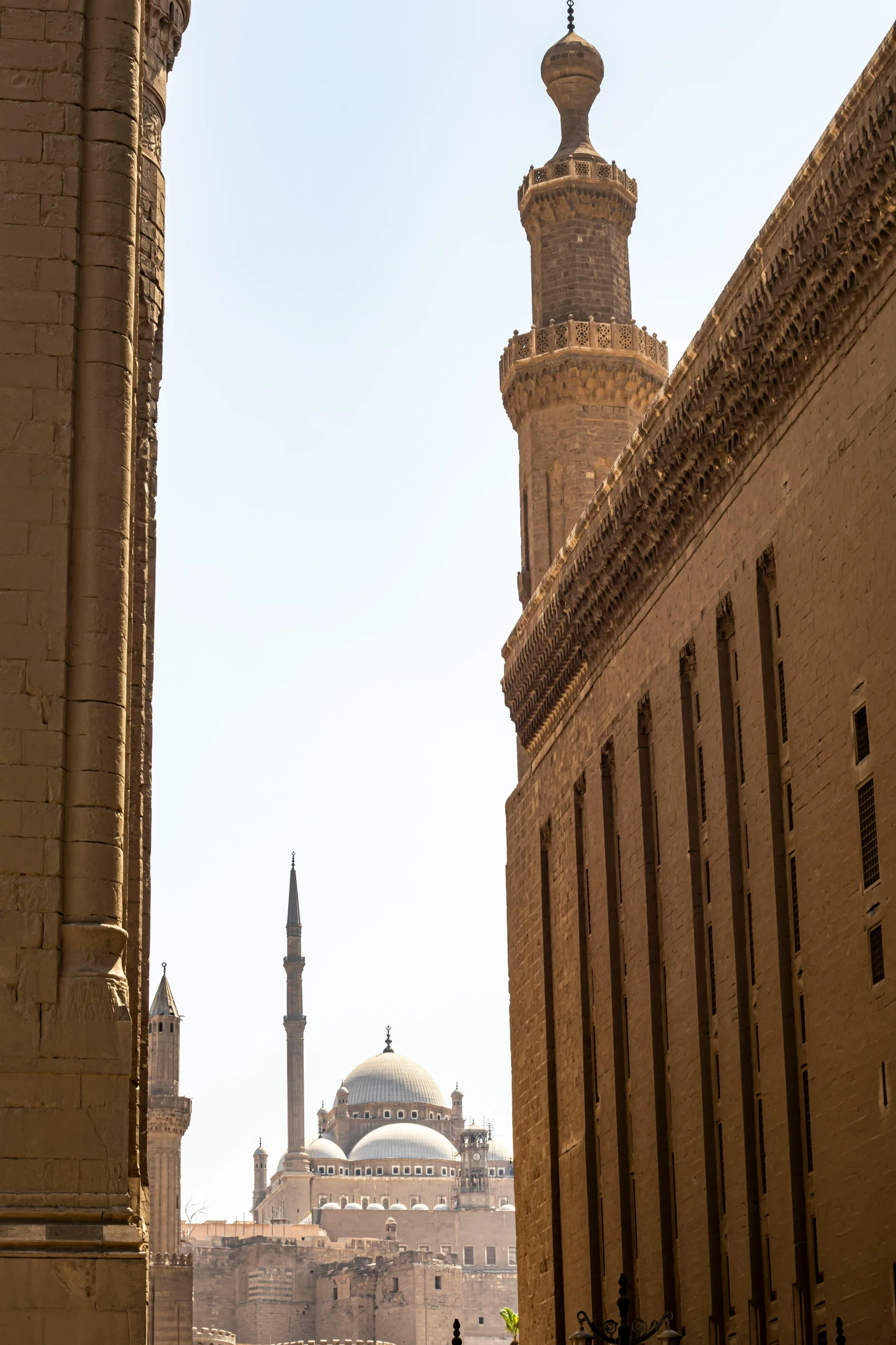 a group of people walking down a street next to tall buildings, by Riad Beyrouti, arabesque, black domes and spires, cairo, seen from a distance, brown