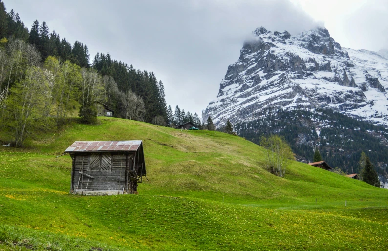 a small cabin sitting on top of a lush green hillside, by Peter Churcher, pexels contest winner, lauterbrunnen valley, mountain snow, barn, conde nast traveler photo