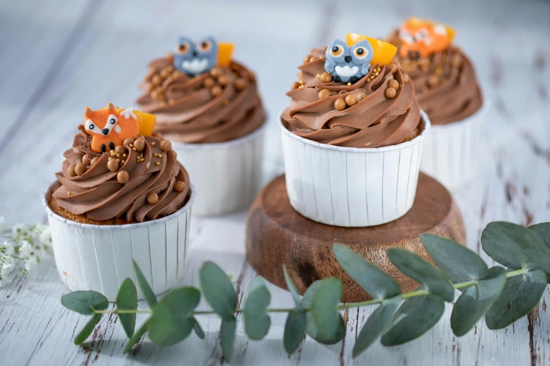 a group of cupcakes sitting on top of a wooden table, a still life, by Helen Stevenson, trending on pexels, owl crown, dark grey and orange colours, 3 woodland critters, close-up product photo
