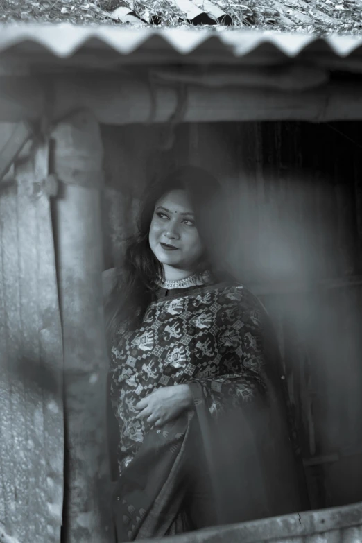 a black and white photo of a woman looking out of a window, by Sunil Das, hurufiyya, standing under a beam of light, ((portrait)), yuli ban, standing outside a house
