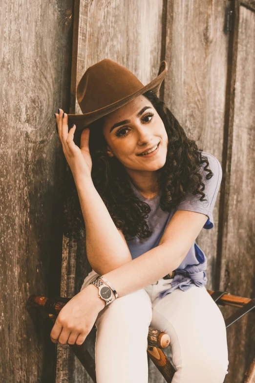 a beautiful young woman sitting on top of a wooden bench, a portrait, by Winona Nelson, pexels contest winner, beige fedora, dark short curly hair smiling, square, cowgirl