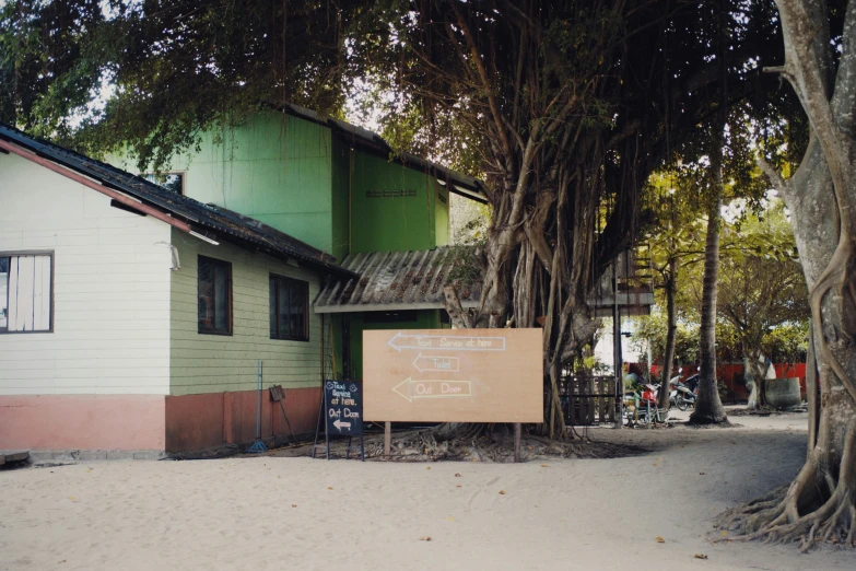 a sign sitting on the side of a road next to a tree, an album cover, unsplash, bengal school of art, beach bar, malaysian, an overgrown library, front view 1 9 9 0