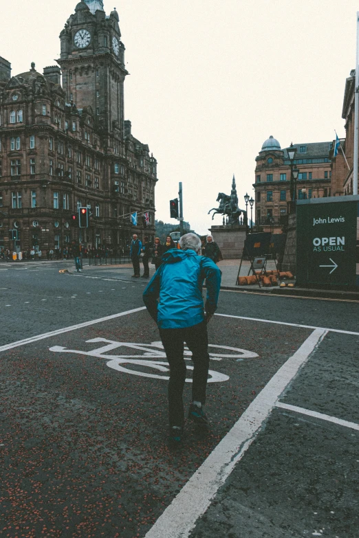 a person walking across a street with a clock tower in the background, by John Murdoch, pexels contest winner, graffiti, glasgow in background, panoramic centered view of girl, square, photo from behind of a cowboy