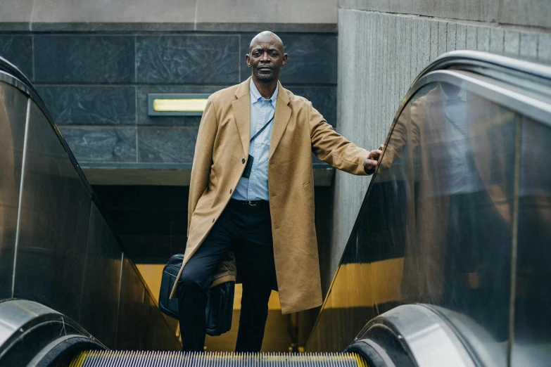 a man that is standing on an escalator, inspired by Harrington Mann, pexels contest winner, figuration libre, light brown trenchcoat, lance reddick, outdoors business portrait, thumbnail