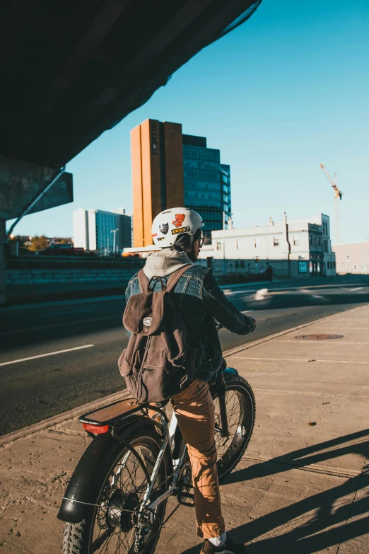 a man standing next to a motorcycle on a city street, a picture, unsplash, happening, wearing skating helmet, view from behind, a man wearing a backpack, bridges