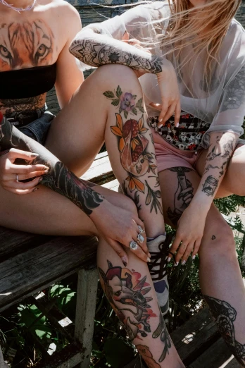 a couple of women sitting on top of a wooden bench, a tattoo, trending on pexels, thigh skin, multi colour, a group of people, arms covered in gang tattoo