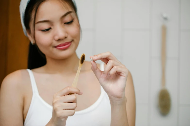 a woman in a white tank top holding a toothbrush, by Nicolette Macnamara, trending on pexels, renaissance, wearing a brown, manuka, asian human, unclipped fingernails