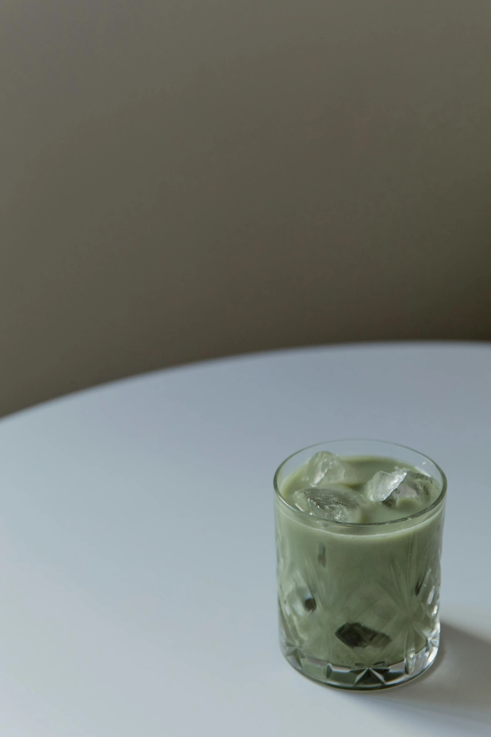 a green drink sitting on top of a white table, a portrait, unsplash, sōsaku hanga, light grey mist, soymilk, ice, ignant