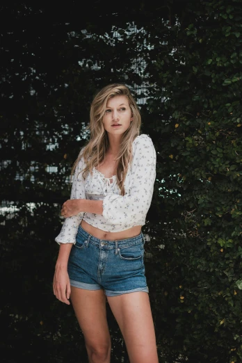 a beautiful young woman standing in front of a bush, by Marshall Arisman, unsplash, wearing denim short shorts, with long blond hair, hollywood promotional image, floral clothes