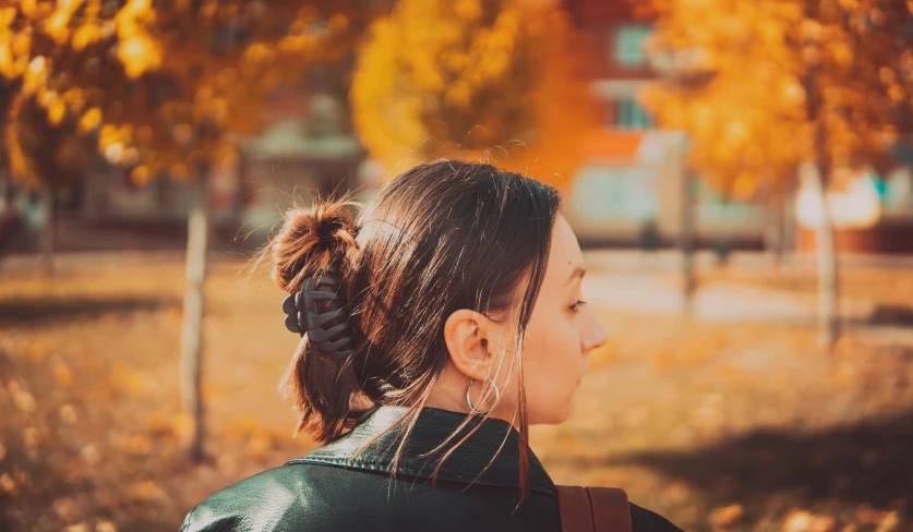 a close up of a person with a backpack, by Emma Andijewska, pexels contest winner, realism, orange and brown leaves for hair, hair tied up in a bun, at a park, profile image