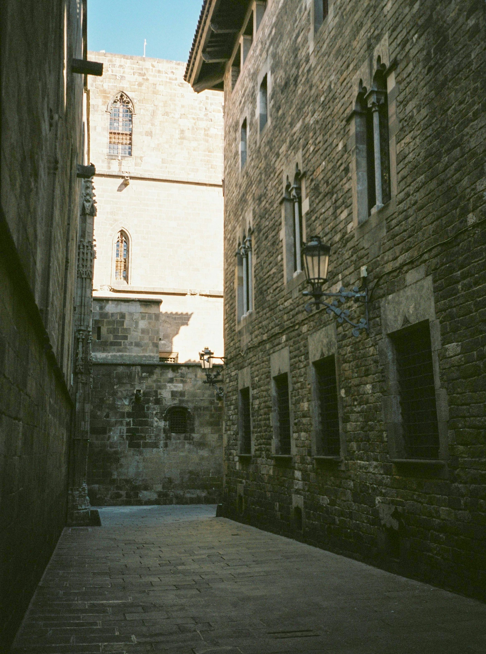 a narrow alley with a clock tower in the background, an album cover, inspired by Modest Urgell, pexels contest winner, romanesque, light academia aesthetic, barcelona, photo taken on fujifilm superia, brutalist courtyard