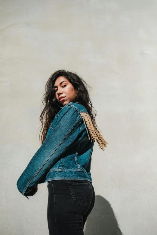 a woman standing in front of a wall wearing a denim jacket, trending on pexels, sza, alanis guillen, profile image, promotional image