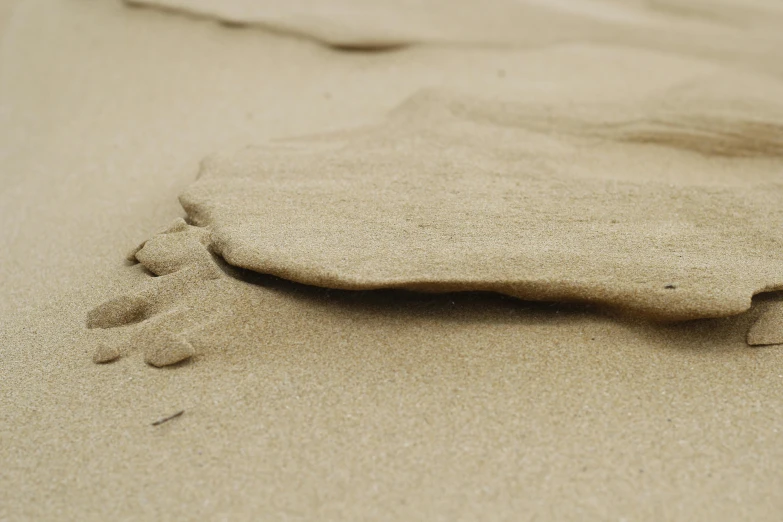 footprints in the sand on a beach, unsplash, land art, sandstone, brown, folds, close up photograph