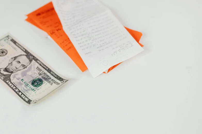 a piece of paper sitting on top of a pile of money, an orange, on a white table, at checkout, lined paper