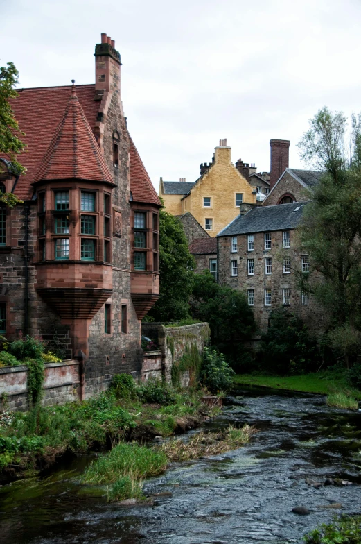 a river running through a small town next to tall buildings, scottish style, inside a castle courtyard, chimneys, lush