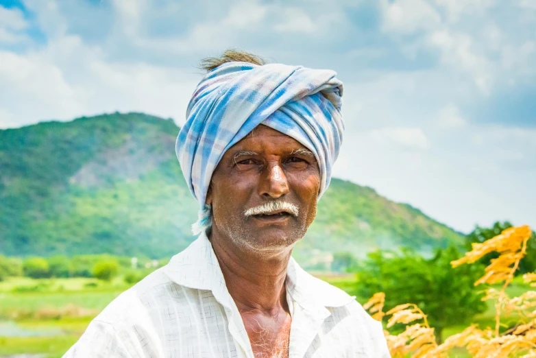 a man with a turban standing in a field, by Scott M. Fischer, pexels contest winner, samikshavad, portrait image, farming, avatar image, standing in front of a mountain