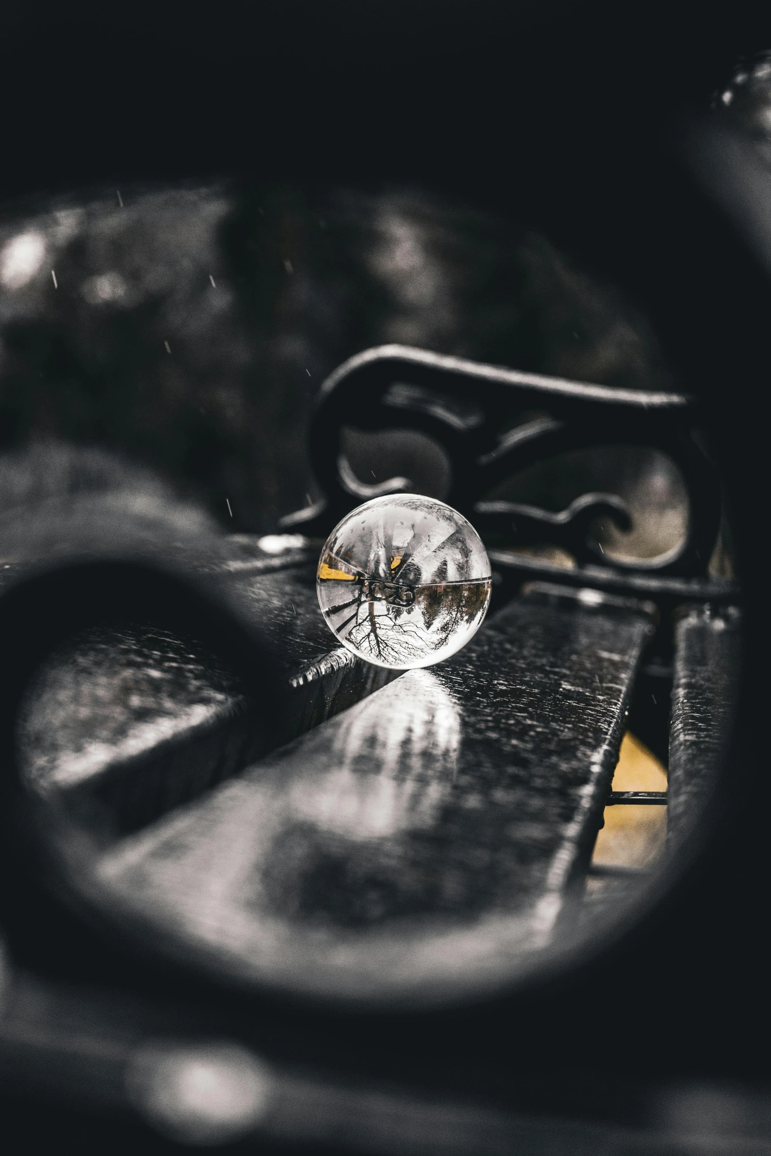 a close up of a glass ball on a bench, by Adam Szentpétery, pexels contest winner, magnifying glass, rainy mood, a high angle shot, medium shot taken from behind