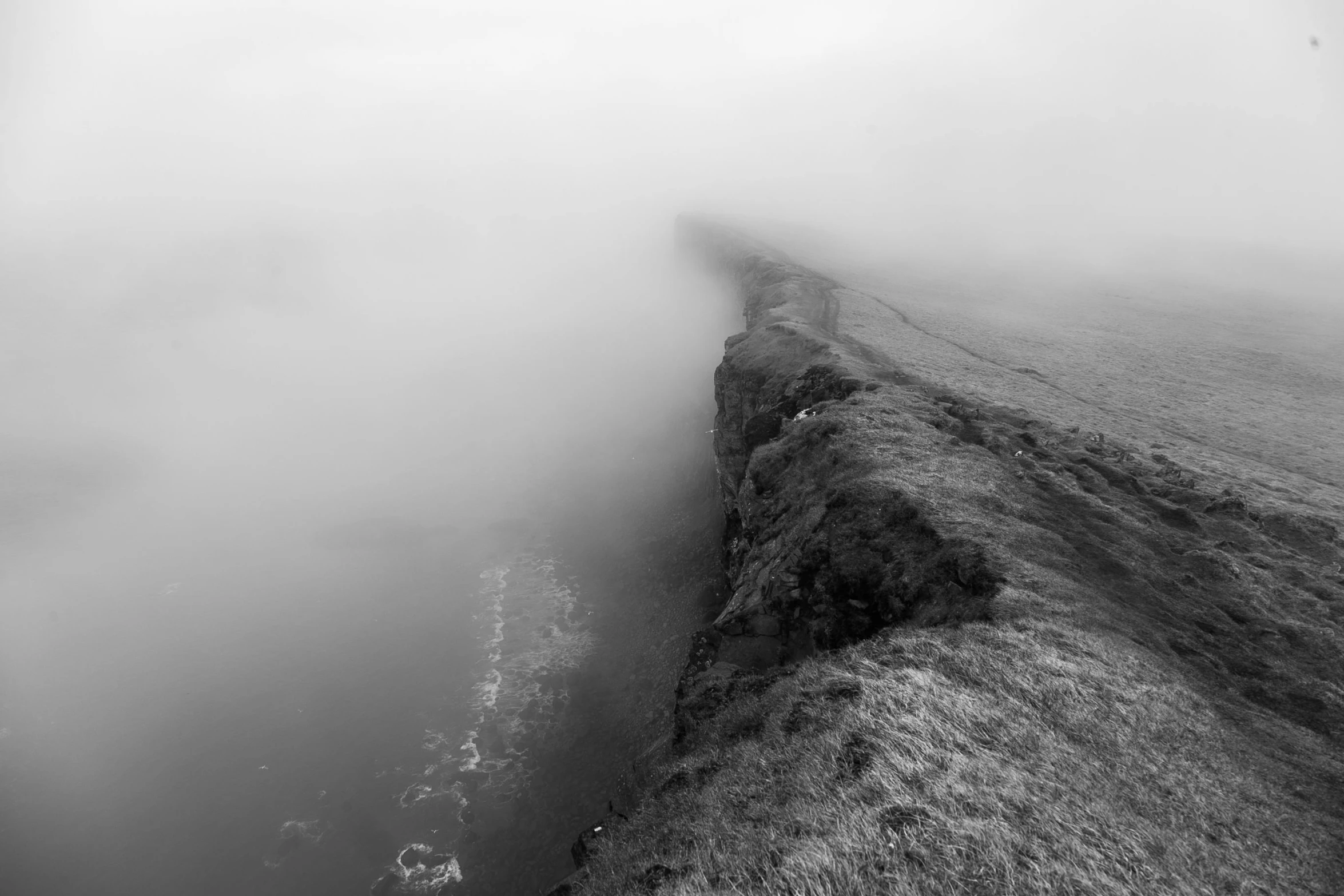 a black and white photo of a foggy beach, a black and white photo, pexels contest winner, looking down a cliff, marsden, foggy swamp, wall