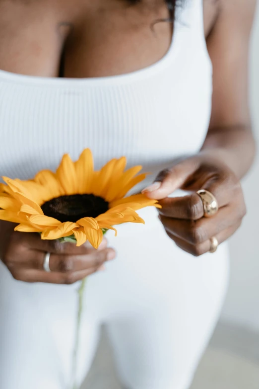 a close up of a person holding a flower, inspired by Sun Long, trending on unsplash, minimalism, pregnant belly, yellow gemstones, dark skinned, set against a white background