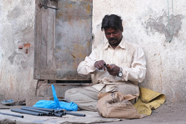a man sitting on the ground in front of a building, pexels contest winner, arte povera, gunsmithing, on an indian street, handheld, thumbnail