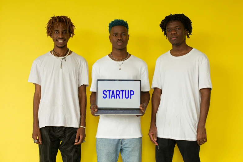 three men standing next to each other holding a laptop, trending on unsplash, afrofuturism, ai startup, wearing a cropped tops, in front of white back drop, starship