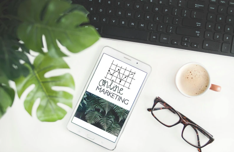 a tablet computer sitting on top of a desk next to a cup of coffee, a picture, by Carey Morris, pexels contest winner, plants in glasses, marketing design, monstera, background image