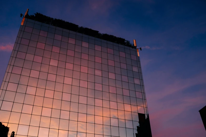 a tall building sitting in the middle of a city, an album cover, unsplash contest winner, modernism, orange / pink sky, glass wall, evening light, tehran