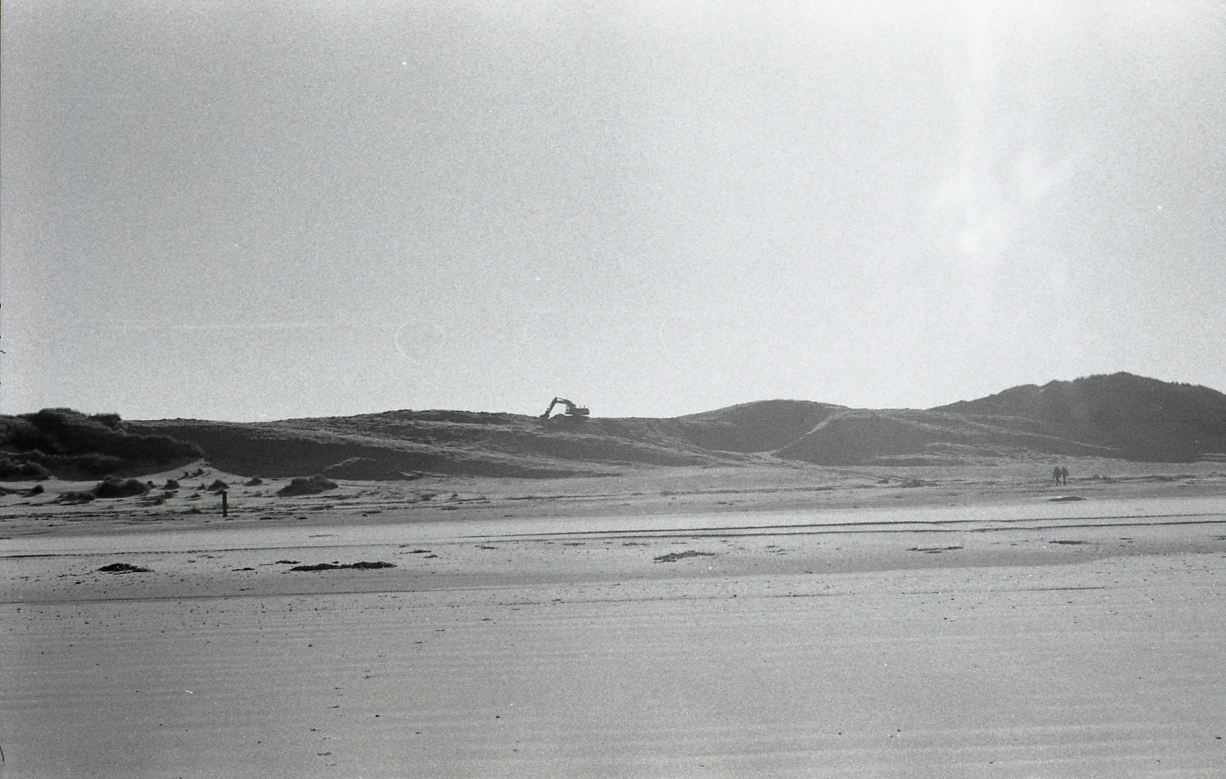 a man flying a kite on top of a sandy beach, a black and white photo, land art, seen from a distance, photo from the dig site, taken on 1970s kodak camera, distant hooded figures