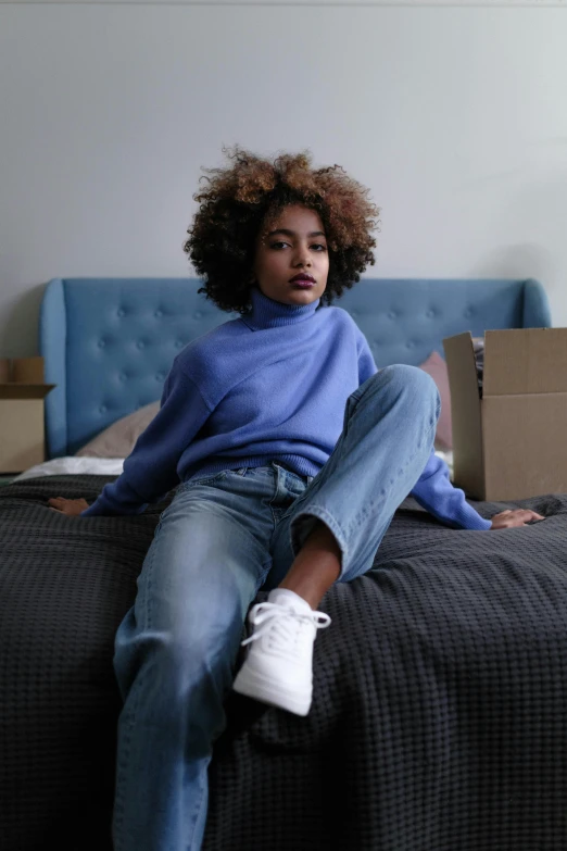 a woman sitting on a bed in a room, by Adam Saks, trending on pexels, happening, blue sweater, ashteroth, wearing white sneakers, promotional image