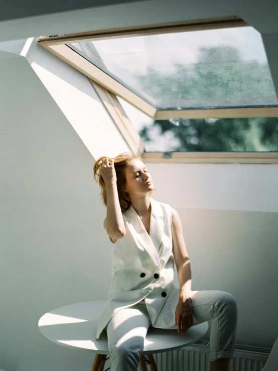 a woman sitting on a chair in front of a window, by Maud Naftel, trending on unsplash, light and space, skylight open ceiling, white waistcoat, aleksandra waliszewska, translucent