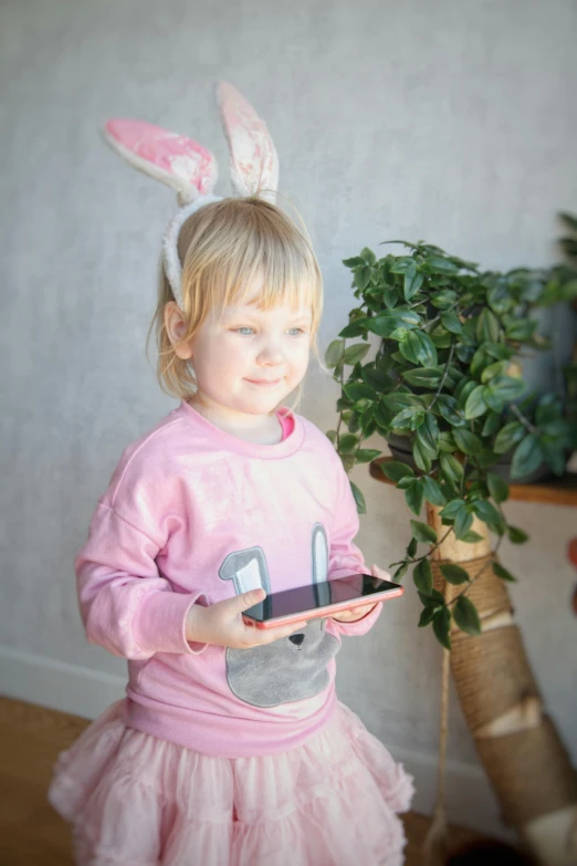 a little girl in bunny ears holding a cell phone, inspired by Beatrix Potter, pexels, wearing a tracksuit, next to a plant, indoor, pink