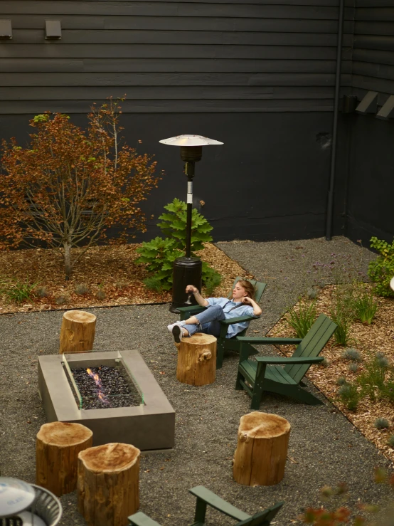 a man sitting in a chair next to a fire pit, by Ben Zoeller, courtyard walkway, ballard, terrarium lounge area, high-resolution photo