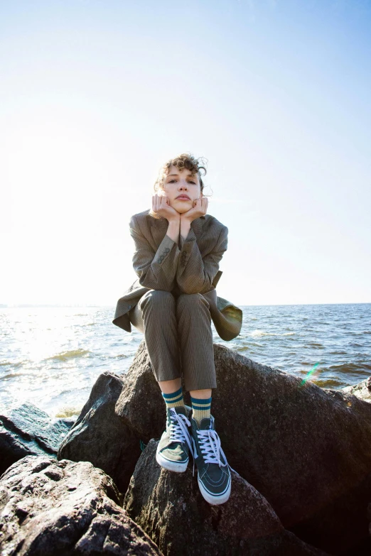 a woman sitting on top of a rock next to the ocean, sophia lillis, girl in suit, genderless, kids