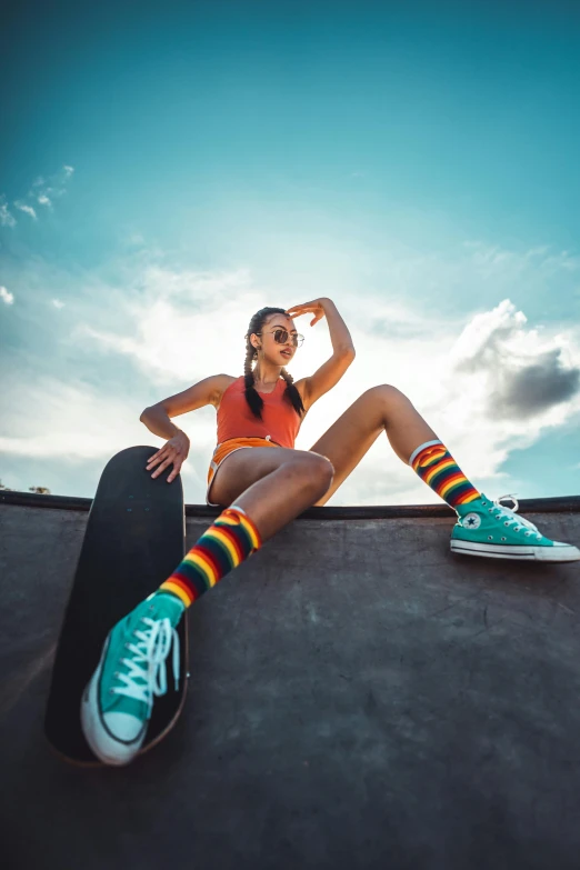 a beautiful young woman sitting on top of a skateboard, by Niko Henrichon, trending on pexels, chartreuse and orange and cyan, striped socks, wearing a tank top and shorts, skies