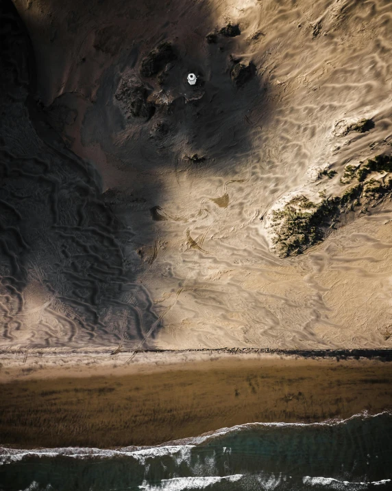a person riding a surfboard on top of a sandy beach, by Jacob Toorenvliet, unsplash contest winner, land art, looking down at a massive crater, hollister ranch, light and dark, slightly pixelated