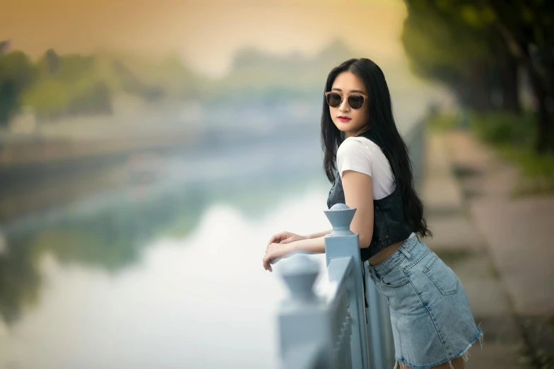 a woman standing next to a body of water, a picture, inspired by Tang Yifen, pexels contest winner, elegant girl in urban outfit, wearing shades, young woman with long dark hair, south east asian with long