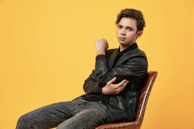 a man in a leather jacket sitting on a chair, trending on pexels, portrait sophie mudd, teenage boy, relaxed posture, hero pose