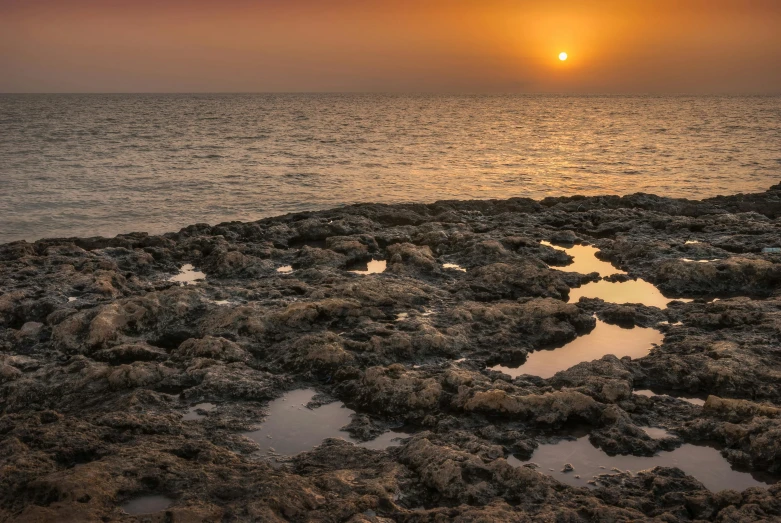 a sunset over the ocean with rocks in the foreground, an album cover, pexels contest winner, romanticism, the dead sea, corals, brown, hd footage