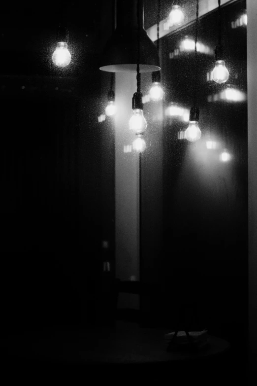 a black and white photo of light bulbs hanging from a ceiling, light and space, late night raining, standing in a dimly lit room, ((mist)), 3 light sources