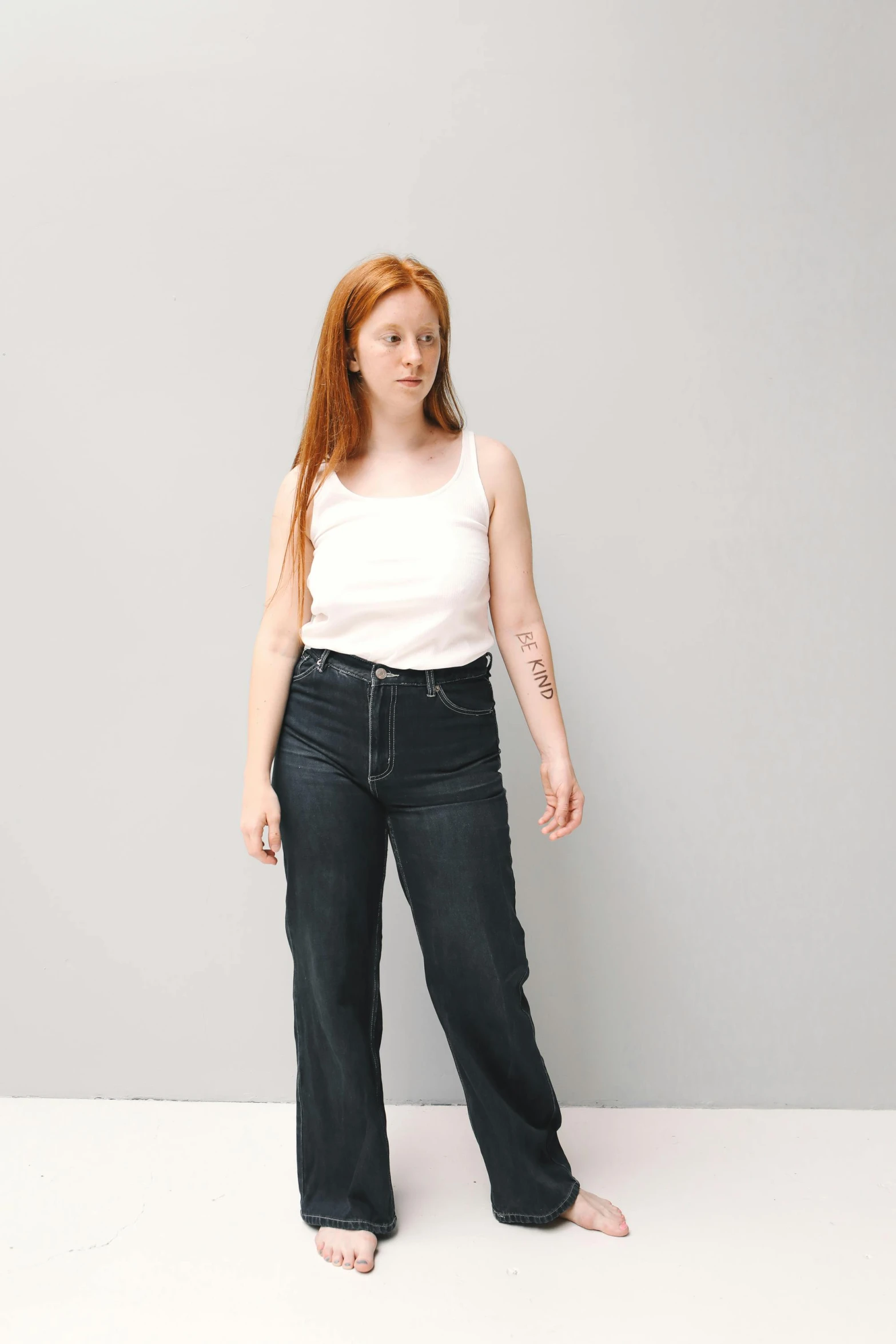 a woman standing in front of a gray wall, featured on reddit, wearing jeans, flowing ginger hair, 2000s photo, wide